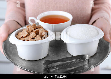 Donna che mantiene il vassoio di metallo con zucchero di bocce e la tazza di tè nero Foto Stock