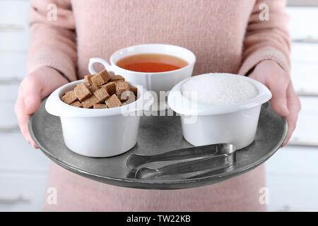 Donna che mantiene il vassoio di metallo con zucchero di bocce e la tazza di tè nero Foto Stock