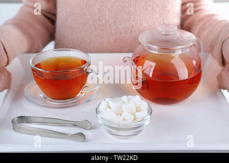 Donna che mantiene il vassoio in legno con zuccheriera, teiera e tazza di tè nero Foto Stock