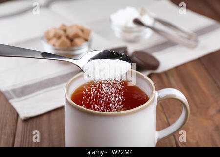 Aggiunta di zucchero per tazza di tè nero sul tavolo di legno Foto Stock