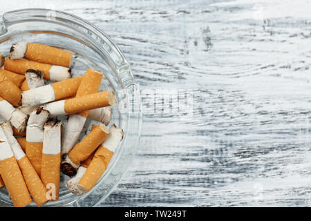 Posacenere in vetro con mozziconi di sigaretta su sfondo di legno Foto Stock