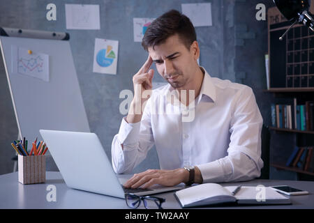 Bel giovane uomo che soffre di mal di testa durante il lavoro in ufficio Foto Stock