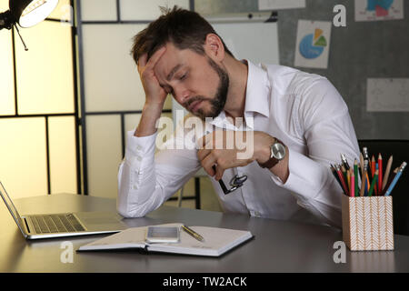 Bel giovane uomo che soffre di mal di testa durante il lavoro in ufficio Foto Stock