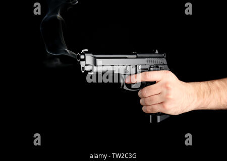 Maschio di mano azienda pistola fumante su sfondo nero Foto Stock