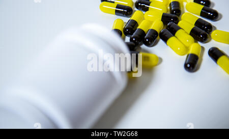 Close up su una bottiglia di farmaci da prescrizione di cadere fuori. Nero e Giallo confetti e compresse medicina isolati su sfondo bianco. Un sacco di medicazione Foto Stock