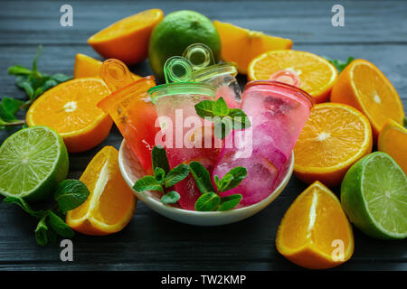Ciotola con deliziosi popsicles di agrumi e frutta fresca sul tavolo di legno Foto Stock