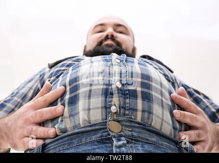 Uomo adulto in piccoli camicia e jeans su sfondo chiaro. La perdita di peso concept Foto Stock