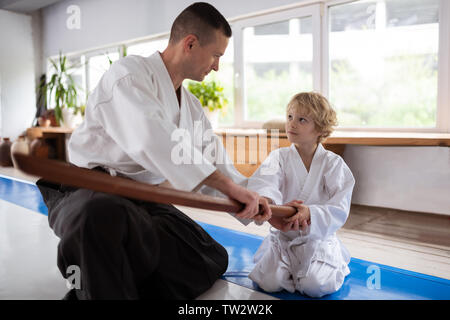 Ragazzo in ascolto. Bionda little boy ascoltando la sua insegnante di aikido seduto vicino alla finestra Foto Stock