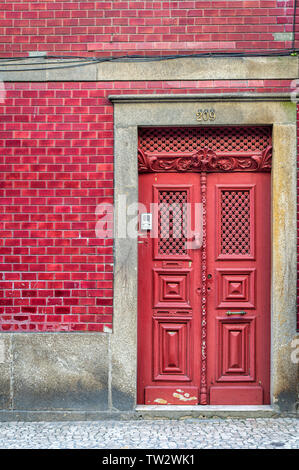 Ornati porta rossa in un rosso edificio piastrellato in Porto, Portogallo. Foto Stock