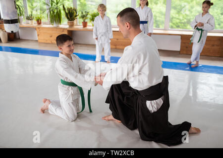 Trainer stringono le mani. Aikido trainer stringe la mano del suo piccolo allievo mentre il supporto di lui prima di mettere in pratica Foto Stock