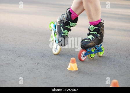 Rullo Сrossed gambe in moto. Rullo di inline skating, roller, slalom sul manto di asfalto. Piccoli coni per la formazione sulla strada. Foto Stock