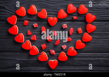 Forma di cuore fatta di gustose caramelle su sfondo di legno Foto Stock
