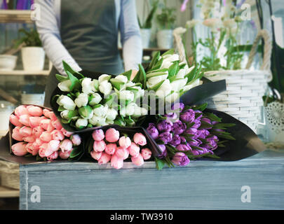 Fiorista femmina in piedi vicino al bancone con bellissimi mazzi di fiori in negozio di fiori Foto Stock