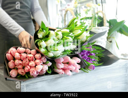 Fiorista femmina in piedi vicino al bancone con bellissimi mazzi di fiori in negozio di fiori Foto Stock