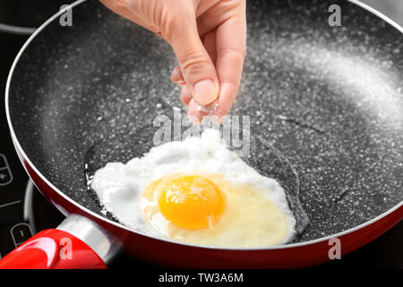 Mano femmina aggiungendo sale a uovo in padella Foto Stock