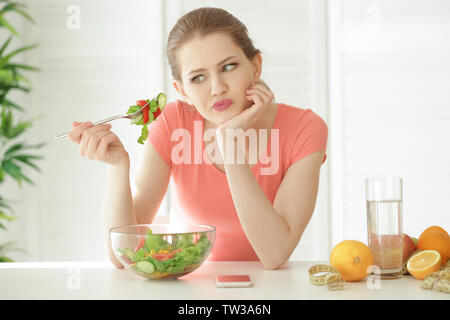 Giovane donna cercando di mangiare insalata in cucina. La perdita di peso concept Foto Stock