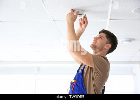 Giovani elettricista installazione rilevatore di fumo sul soffitto Foto Stock