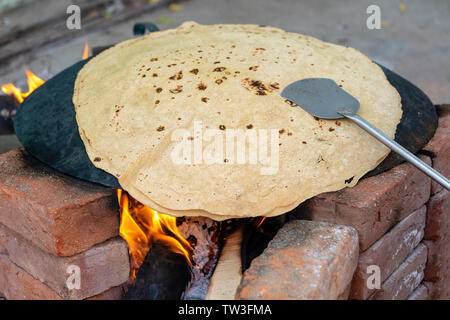 Donna indiana per la cottura tradizionale pane indiano, big chapati per la cottura sul fuoco aperto in Udaipur, Rajasthan, India. Close up Foto Stock