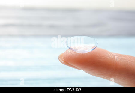 Dito femmina con lente a contatto su sfondo sfocato Foto Stock