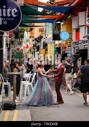 Una giovane coppia in Singapore posa per foto professionali in Haji Lane vestito in un colorato tipo di nozze abiti guardato da membri del pubblico. Foto Stock