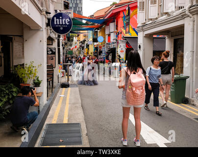 Una giovane coppia in Singapore posa per foto professionali in Haji Lane vestito in un colorato tipo di nozze abiti guardato da membri del pubblico. Foto Stock
