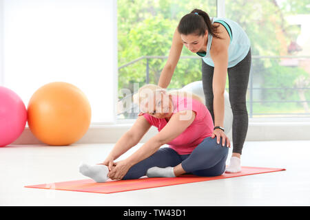 Istruttore senior ad aiutare la donna a praticare lo yoga in palestra Foto Stock