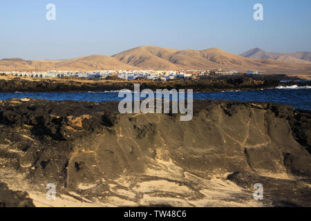 El Cotillo: Vista su rocce di origine vulcanica e la laguna blu sul villaggio bianco secco con marrone colline a nord di sfondo Fuerteventura Foto Stock