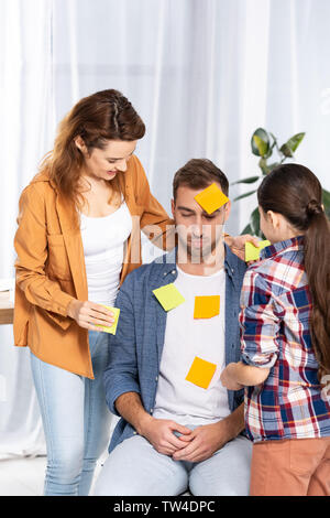 Donna felice e kid mettendo yellow sticky notes su sconvolto l'uomo Foto Stock