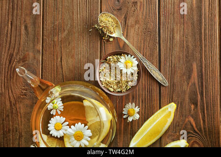 Composizione con la camomilla tè nella teiera in vetro su sfondo di legno Foto Stock