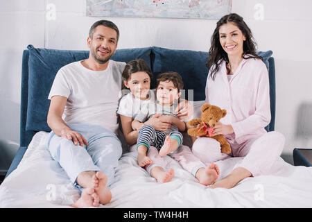 Allegro con la famiglia a piedi nudi seduti sul letto e sorridere mentre guardando la fotocamera Foto Stock