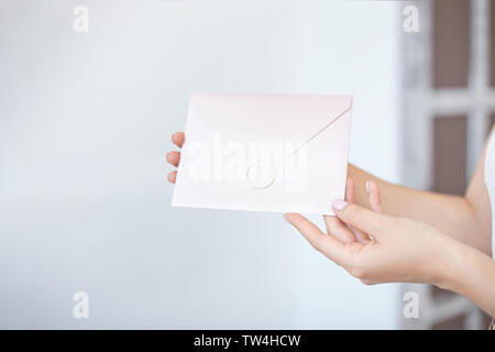 Close-up foto di mani femminili tenendo un blu argento o rosa Busta invito con un sigillo di cera, un certificato regalo, una cartolina, un invito a nozze Foto Stock