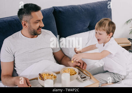Allegro padre e figlio avente la prima colazione durante la permanenza a letto insieme Foto Stock