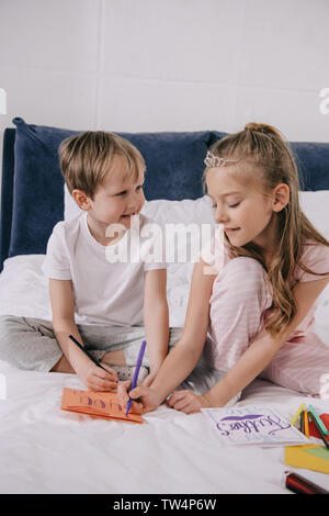 Adorabili bambini disegno padri giorno saluto automobili mentre seduto sul letto Foto Stock