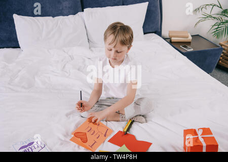 Carino ragazzo che padri giorno biglietto di auguri con ti amo papà iscrizione e il simbolo del cuore mentre è seduto sul letto vicino a confezione regalo Foto Stock