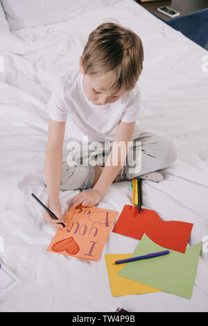 Carino ragazzo che padri giorno biglietto di auguri con ti amo papà iscrizione e il simbolo del cuore mentre è seduto sulla biancheria da letto Foto Stock