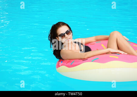 Bella giovane donna sulla ciambella gonfiabile in piscina Foto Stock