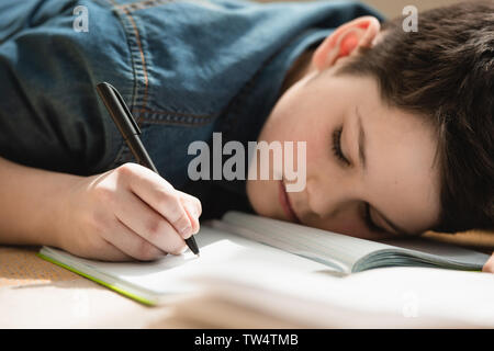 Esaurito il ragazzo disteso sul pavimento e la scrittura nella copia di un libro mentre facendo i compiti a casa Foto Stock