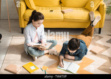 Elevato angolo di vista adorabili bambini facendo i compiti sul pavimento a casa Foto Stock