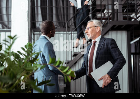 Basso angolo di visione dell uomo d affari stringono le mani con african partner americano Foto Stock