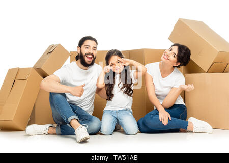 Felice l'uomo latino che mostra il pollice fino nei pressi di kid gesticolando e moglie sorridente vicino a scatole isolato su bianco Foto Stock