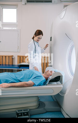 Attraente medico sorridente preparando l'uomo per la scansione nella macchina MRI Foto Stock