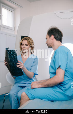 Bella medico guardando a raggi x diagnosi vicino al paziente seduto su scanner MRI bed Foto Stock