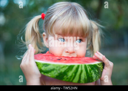 Ritratto di bella bionda bambina con due ponytails e occhi blu mangiando anguria. Kid mangia frutta. Foto Stock