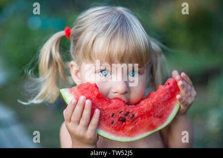 Ritratto di bella bionda bambina con due ponytails e occhi blu mangiando anguria. Kid mangia frutta. Foto Stock