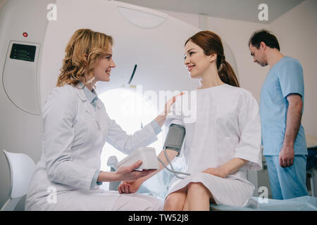 Sorridente medico pazienti di misurazione della pressione sanguigna con il tonometro di assistente durante la regolazione dello scanner TC Foto Stock