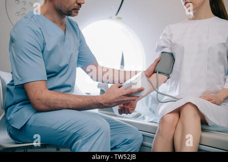 Vista parziale del medico i pazienti di misurazione della pressione sanguigna con tonometro seduti a CT scanner Foto Stock