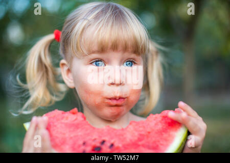 Ritratto di bella bionda bambina con due ponytails e occhi blu mangiando anguria. Kid mangia frutta. Foto Stock