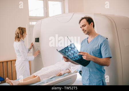 Attento medico guardando la diagnosi di tomografia mentre il radiologo di funzionamento dello scanner TC durante la diagnosi dei pazienti Foto Stock