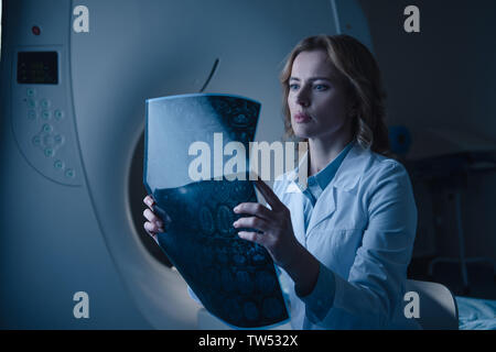 Bella medico guardando a raggi x diagnosi mentre è seduto vicino a Computed Tomography scanner Foto Stock