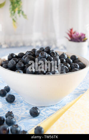 I mirtilli freschi raccolti riempiono la ciotola bianca in un ambiente luminoso e luminoso della cucina. Foto Stock